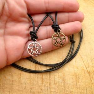 May include: Two leather necklaces with silver and gold pentagram pendants. The necklaces are black and the pendants are both silver with a five-pointed star.