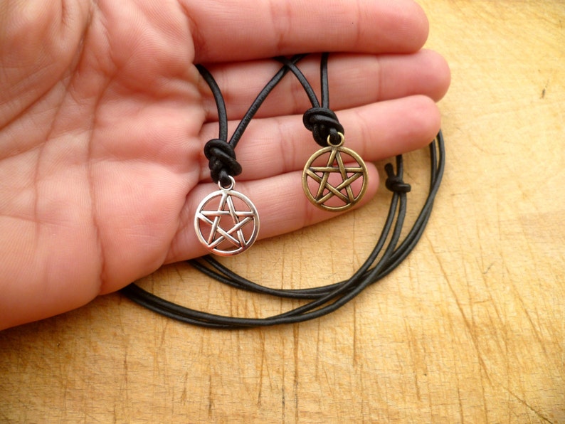 May include: Two leather necklaces with silver and gold pentagram pendants. The necklaces are black and the pendants are both silver with a five-pointed star.