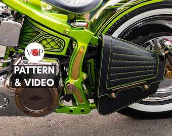 May include: A green motorcycle with a black leather saddlebag with yellow stitching. The motorcycle has a gold-colored frame and a black and white tire. The saddlebag has a brass buckle and a brass plate with the text "V&P PATTERN & VIDEO".