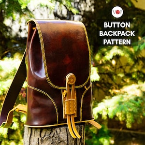 Puede incluir: Una mochila de cuero marrón con cierre de botón y costuras amarillas. La mochila tiene una correa que va sobre el hombro y una correa más pequeña que va cruzada por el pecho. La mochila está sentada sobre un tocón de árbol.