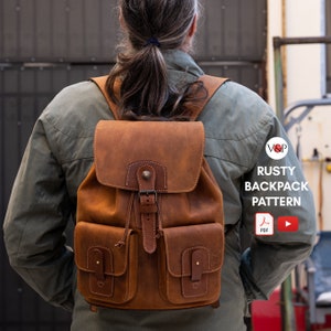 Könnte beinhalten: Ein brauner Lederrucksack mit zwei Fronttaschen und einem Schnallenverschluss. Der Rucksack wird von einer Person mit langen braunen Haaren getragen. Der Text "RUSTY BACKPACK PATTERN" ist im Bild sichtbar.