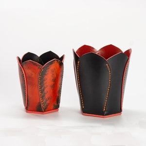 May include: Two leather flower pot holders, one black and one orange with black accents. Both have a tulip shape.