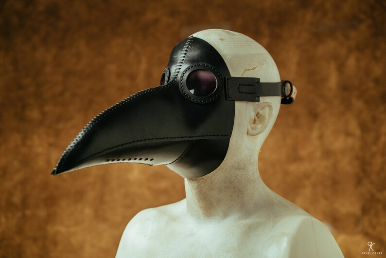 May include: A black leather plague doctor mask with a long beak and goggles. The mask is worn on a mannequin's head.
