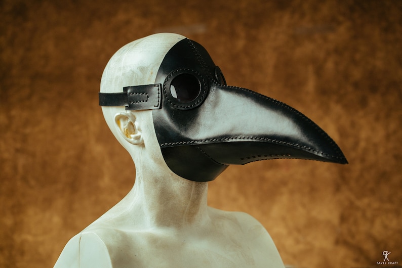 May include: A black leather plague doctor mask with a long beak and eye holes. The mask is worn on a mannequin's head.
