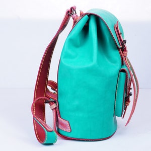 May include: A turquoise leather backpack with red stitching and a small front pocket. The backpack has a drawstring closure and adjustable straps.