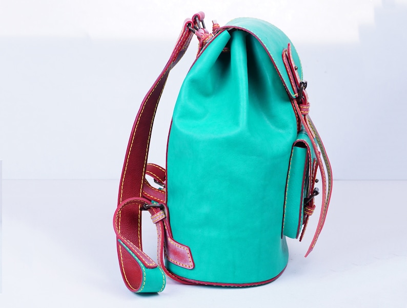 May include: A turquoise leather backpack with red stitching and a small front pocket. The backpack has a drawstring closure and adjustable straps.