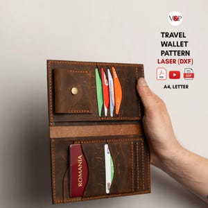 May include: Open brown leather travel wallet with multiple card slots and a passport pocket. The wallet is held open, displaying colourful cards and a Romanian passport. The text "TRAVEL WALLET PATTERN LASER (DXF)" is visible.