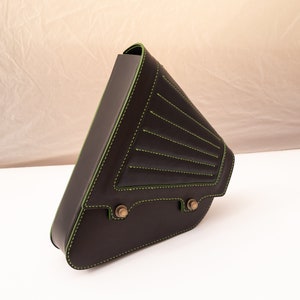 May include: A brown leather motorcycle saddlebag with green stitching. The bag has a triangular shape and a flap closure.