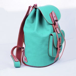 May include: A teal blue leather backpack with brown leather straps and a buckle closure. The backpack has a small front pocket with a flap and a drawstring closure.