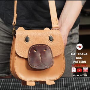 May include: A tan leather shoulder bag shaped like a capybara with a dark brown snout, black eyes, and a long strap. Text on the right reads: V&P CAPYBARA BAG PATTERN LASER (DXF) PDF, YouTube icon, DXF icon, A0, A4, LETTER.