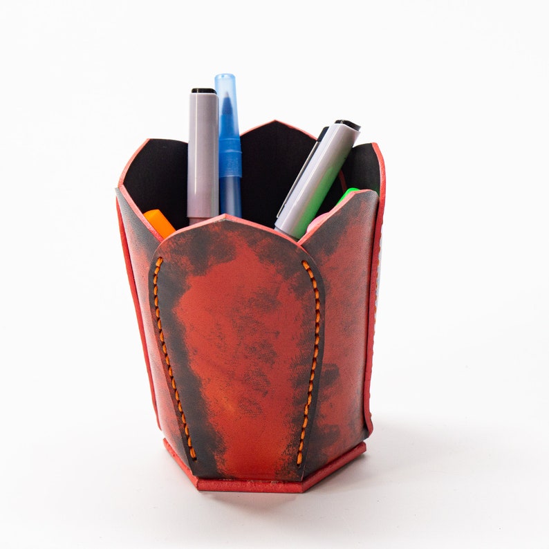 May include: Red leather pen holder shaped like a flower with a distressed finish. The holder has several pens and markers inside.