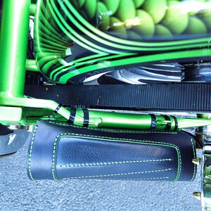 May include: A close-up of a green motorcycle with black stripes and a black leather saddlebag. The motorcycle has a green and black paint job and a black leather saddlebag with green stitching.