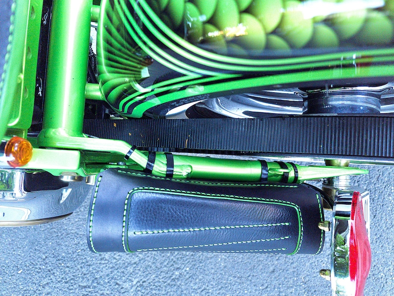 May include: A close-up of a green motorcycle with black stripes and a black leather saddlebag. The motorcycle has a green and black paint job and a black leather saddlebag with green stitching.