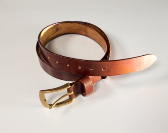 May include: A brown leather belt with a brass buckle. The belt is folded in half and the buckle is visible.