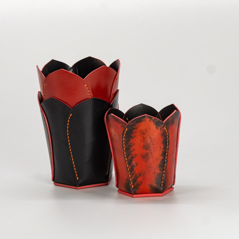 May include: Two leather flower pot holders, one black and one red, with orange stitching.