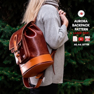 Könnte beinhalten: Ein brauner Lederrucksack mit hellbraunem Boden und Akzenten. Der Rucksack hat einen Klappenverschluss mit Schnalle und einen Kordelzug oben. Der Text "AURORA BACKPACK PATTERN" ist sichtbar.