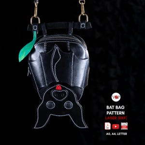 Puede incluir: Un bolso de cuero negro con forma de murciélago colgante, costuras blancas, detalle de nariz roja y herrajes de latón. El texto dice V&P BAT BAG PATTERN LASER (DXF) con iconos de PDF, YouTube, DXF y A0, A4, LETTER.