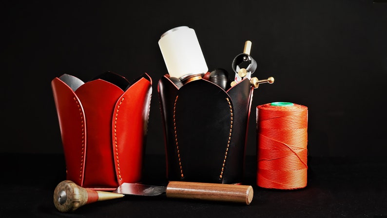May include: Three red leather tulip-shaped containers, one with a black leather container filled with tools, a spool of red thread, and a wooden tool.