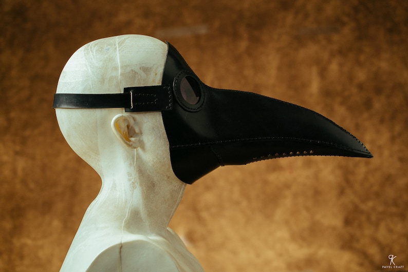 May include: A black leather plague doctor mask with a long beak and a round eye piece. The mask is worn on a mannequin head.