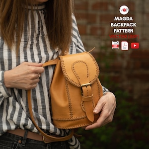 Peut inclure: Un sac à dos en cuir tanné avec une fermeture à boucle et des coutures décoratives. Le sac à dos a une sangle qui passe par-dessus l'épaule. Le sac à dos est tenu par une personne portant une chemise rayée.