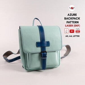 Op de afbeelding: Een lichtblauwe leren rugzak met een donkerblauwe riem en gesp. De tas heeft een voorvak en een handvat aan de bovenkant. De tekst "AZURE BACKPACK PATTERN LASER (DXF)" is zichtbaar.