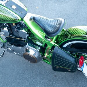 May include: A green motorcycle with a black leather seat and a black leather saddlebag. The motorcycle has a chrome engine and a white wall tire. The motorcycle has a green and black paint job with a fish scale pattern.