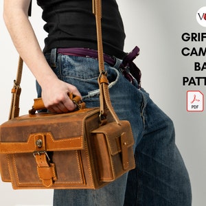 Peut inclure: Un sac à appareil photo en cuir marron avec une bandoulière et une petite poche sur le côté. Le sac est tenu par une personne portant un jean. Le texte "GRIFFITH CAMERA BAG PATTERN" est visible sur l'image.