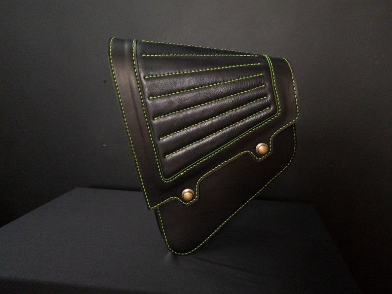 May include: Black leather motorcycle saddlebag with green stitching and brass accents.