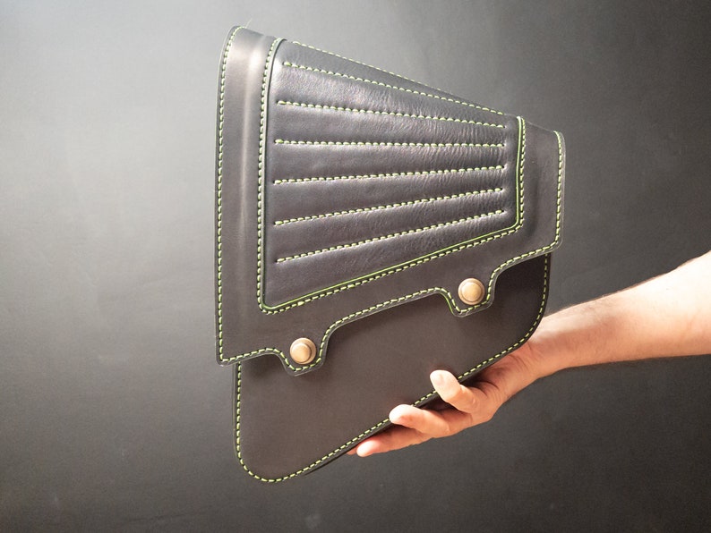 May include: A black leather motorcycle saddlebag with green stitching and metal accents.
