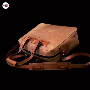 May include: A brown leather briefcase with a strap and buckle closure. The bag has a top handle and a shoulder strap.