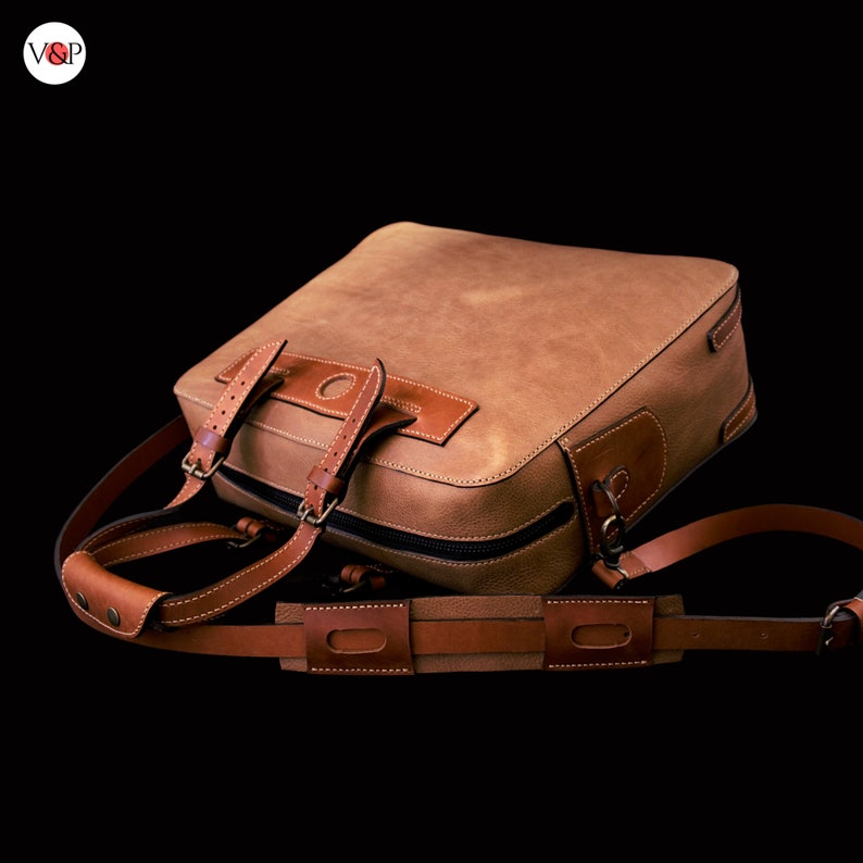 May include: A brown leather briefcase with a strap and buckle closure. The bag has a top handle and a shoulder strap.