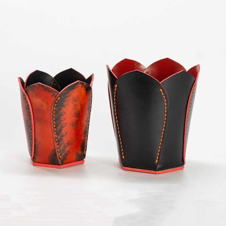May include: Two leather flower pot holders, one black and one orange with black accents. The pots are shaped like tulips.