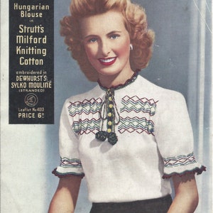 May include: Vintage magazine cover featuring a woman wearing a white Hungarian blouse. The blouse has intricate embroidery in green, red, and blue, with a high collar and short sleeves. The text reads "Strutt's Milford Knitting Cotton".