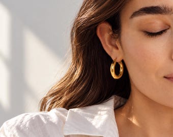 May include: A thick, polished gold hoop earring with a smooth, rounded surface. The earring features a circular design that sits securely in the earlobe, reflecting light with a bright, metallic finish and a substantial, chunky profile.