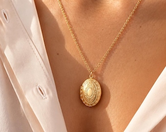 May include: A gold-toned oval locket pendant suspended from a delicate matching gold-toned chain. The locket features an intricate embossed floral pattern surrounding a smooth, plain oval center panel, creating a classic and detailed appearance.