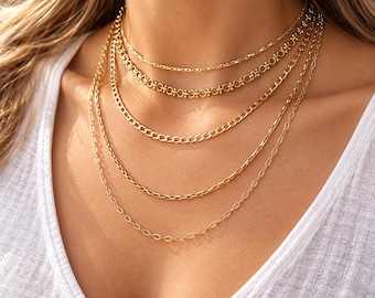 May include: A layered gold necklace set consisting of five distinct chains of varying lengths and link styles. The collection includes a delicate cable chain, a textured link chain, a classic curb chain, a decorative station chain, and a thin chain.