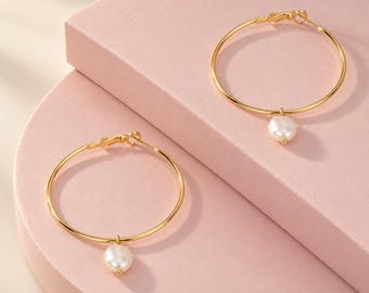 May include: A pair of gold-toned hoop earrings, each featuring a single white, irregular-shaped pearl charm suspended from the bottom of the thin circular wire frame. The earrings include a hinged clasp mechanism at the top for secure closure.
