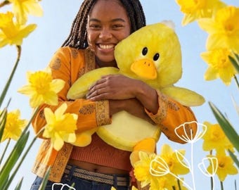 May include: A bright yellow plush duck toy with a rounded head, small orange beak, and soft texture. The duck features large black eyes and is held against a person wearing a mustard yellow patterned jacket and dark blue denim jeans.