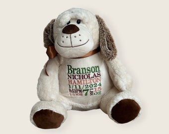 May include: A cream-colored plush dog with brown ears and paws, wearing a brown ribbon around its neck. The chest is embroidered with the name Branson Nicholas Hamilton, the date 1/11/2024, 8:53PM, and 7 lbs 15 oz, 19 1/2 inches.