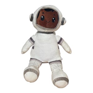 May include: A plush astronaut doll in a white spacesuit with gray accents. The doll has a brown face with a smiling expression and a white helmet with gray details. The toy is designed for children.