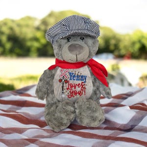 May include: A gray teddy bear wearing a striped conductor hat and a red scarf. The bear has an embroidered design on its chest with the words "Yenny Loves You!" and a railroad crossing sign.