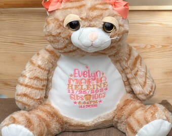 May include: A plush orange tabby cat toy with white paws and a white chest patch. The cat wears two peach-colored bows on its ears. The chest features embroidered text: Evelyn, Maria, Heleine, 11/25/2024, 6lbs 10oz, 6:04PM, and 18.5 inches.