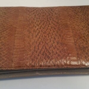 K&ouml;nnte beinhalten: Eine braune Leder-Clutch mit einem strukturierten Muster. Die Clutch hat einen Klappverschluss und ein kleineres Fach unten.