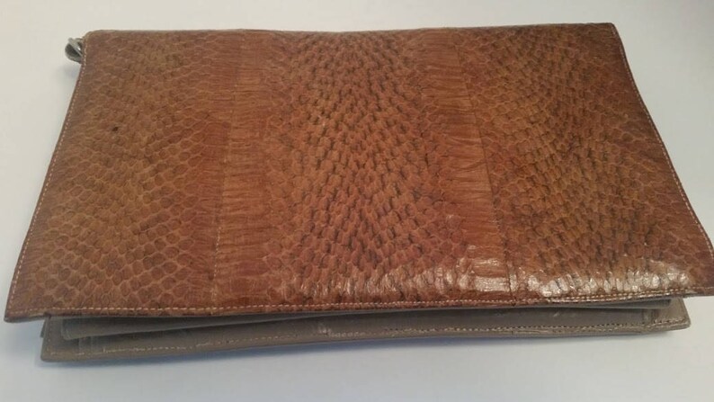 K&ouml;nnte beinhalten: Eine braune Leder-Clutch mit einem strukturierten Muster. Die Clutch hat einen Klappverschluss und ein kleineres Fach unten.