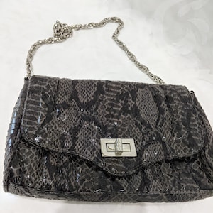 May include: A black snakeskin-patterned handbag with a silver chain strap and a silver clasp closure.