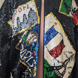 May include: A black sequined bomber jacket with a zipper closure. The jacket features colorful patches with the words "London", "Paris", and other designs.