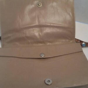 K&ouml;nnte beinhalten: Eine beige Lederhandtasche mit Klappenverschluss und einer kleinen Tasche auf der Vorderseite. Die Tasche hat einen braunen Lederriemen.