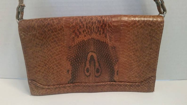 K&ouml;nnte beinhalten: Eine braune Lederschultertasche mit Schlangenhautmuster. Die Tasche hat einen Klappenverschluss und einen einzigen Riemen.
