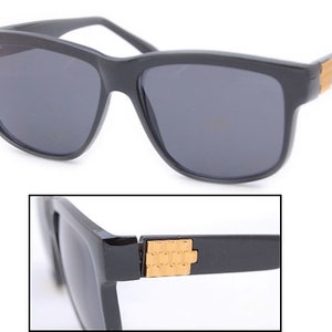 May include: Black square-shaped sunglasses with dark lenses and gold accents on the arms.