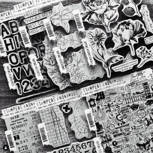 May include: A collection of clear rubber stamps featuring various designs, including floral patterns, alphabet letters, numbers, and vintage-inspired graphics. The stamps are arranged on a black and white background with text that reads "Stampers Anonymous" and includes a phone number and website address.